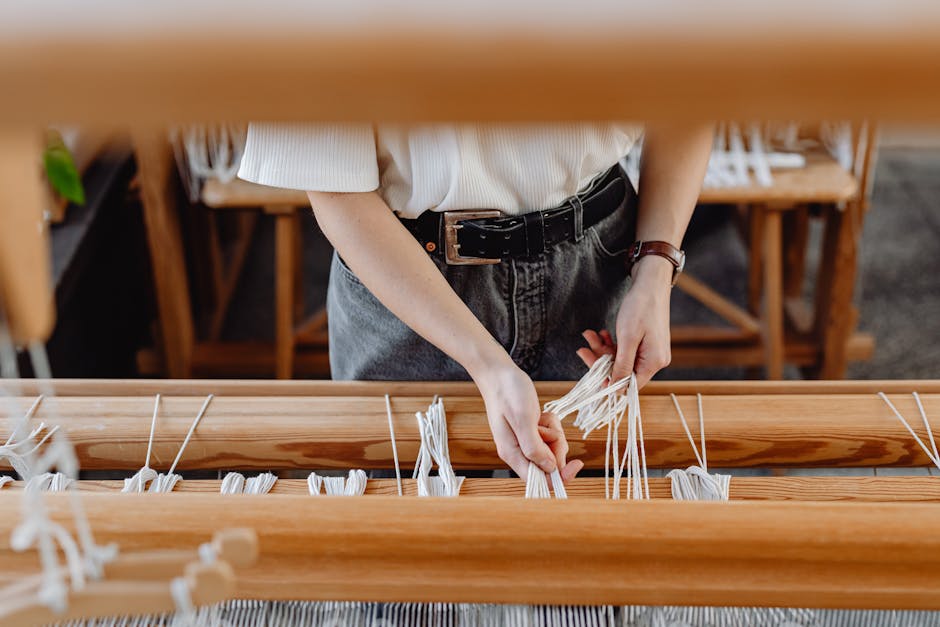 Close-up of hands weaving on a traditional wooden loom in a workshop.