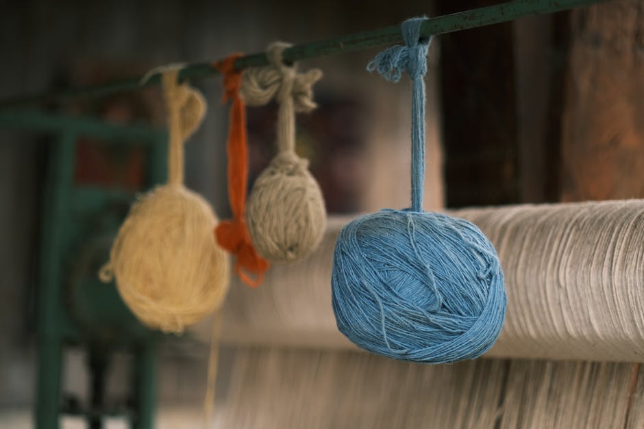 Vibrant blue, orange, and beige yarn balls hanging in a loom workshop, symbolizing creative textile design.