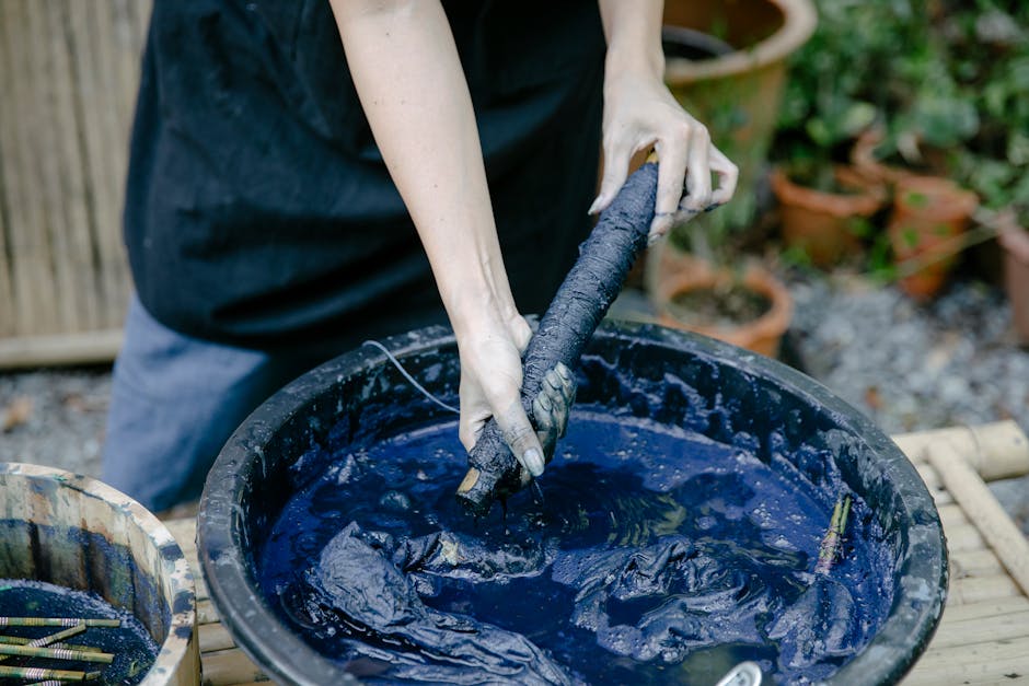 A close-up of hands dyeing fabric with indigo dye outdoors, emphasizing traditional techniques.